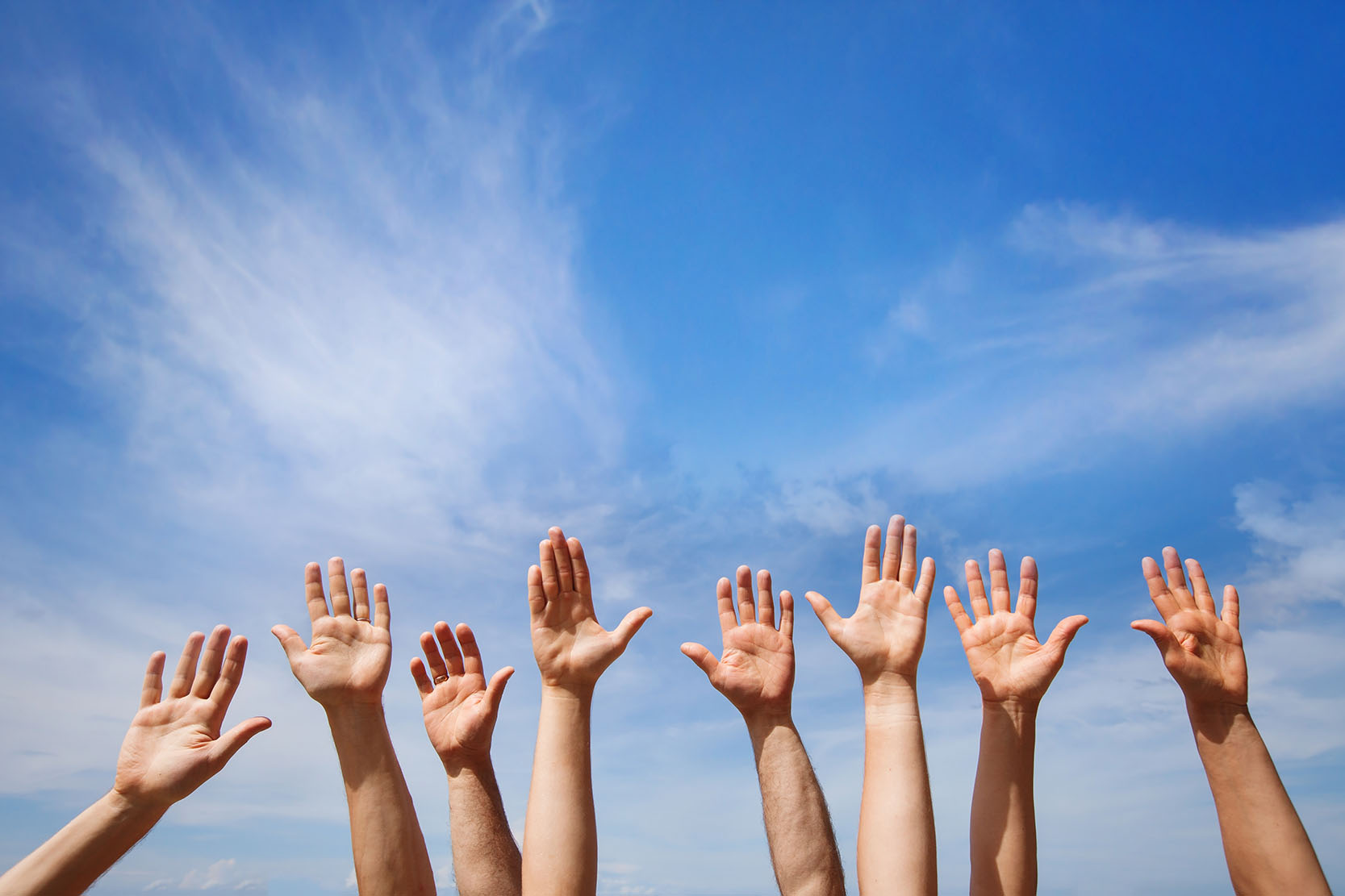 Raised hands against blue sky background
